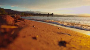 Gün batımında Issyk kul Gölü 'nde bir balıkçıyla iskelede. Kırgızistan 'da dalgalar ve kumlu plaj