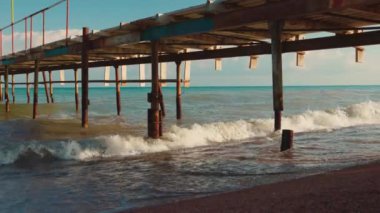 Gün batımında Issyk-kul Gölü 'nde dalgaları olan boş kumlu sahildeki eski ahşap iskele. Yazın Kırgızistan 'daki Kaji Sai köyü.