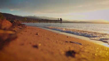 Issyk kul Gölü 'nde gün batımında iskelede balıkçılar ve arka planda dağlarla. Kırgızistan 'da dalgalar ve kumlu plaj
