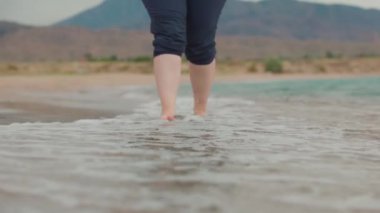 Issyk-kul Gölü 'nde kumsalda yürüyen bir kadın. Denizde kadın bacaklarını kapat. Kırgızistan 'da yaz zamanı Tosor köyü.