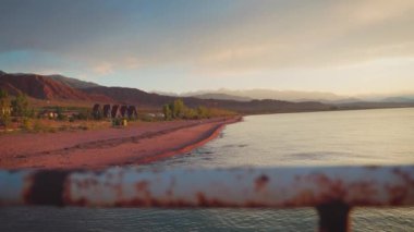 Gün batımında Issyk-kul Gölü 'nde küçük dalgalar ve arka planda dağlar olan boş kumlu bir sahil. Yazın Kırgızistan 'daki Kaji Sai köyü.