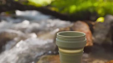 Kadın yeşil kupaya Drip Coffee Bag koymuş. Yaz ormanlarındaki dağ nehrinin yakınındaki kayalıklarda demlenen içecek işlemleri..