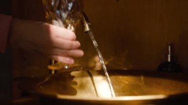 Kadının, mutfak lavabosundaki musluktan akan suyla yakın çekim görüntüsü. Sabah ışığı köy evinin odasında..