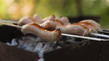 Barbeküdeki sosisler piknik bahçesinde duman ve alevlerle kaplıdır.