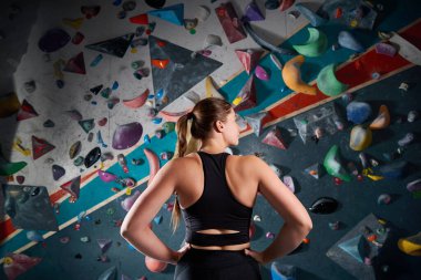 Sportsman athlete climber young woman standing back against steep wall in climbing gym indoors. Extreme sports and bouldering concept clipart