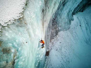 Turuncu ceketli sporcunun hava aracı görüntüsü Kazakistan 'daki dağ vadisinde buzdan büyük bir duvara tırmanıyor.