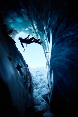 Siyah siluetli adam buz baltası ve kramponlarla buz dağlarındaki donmuş buz mağarasına tırmanıyor. Spor dağcılığı ve dağcılık konsepti