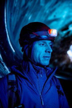 Dağcı, kırmızı miğferli, parlak farlı, koyu buzul mağarasında mavi ışıklı dağcı Kazakistan 'daki kış buzullarını keşfediyor.