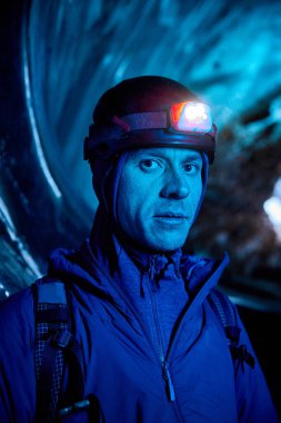 Dağcı, kırmızı miğferli, parlak farlı, koyu buzul mağarasında mavi ışıklı dağcı Kazakistan 'daki kış buzullarını keşfediyor.