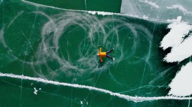 Havadan insansız hava aracı, sarı ceketli bir adamın donmuş gölde buz pateni yaparken, kışın çatırtı ve karla kaydığını gösteriyor.