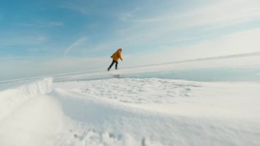 Sarı ceketli bir adamın kışın donmuş gölde buz pateni yaparken ki görüntüsünü takip edin.