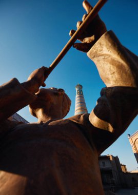 Özbekistan 'ın Itchan Kala antik kenti Khiva' da flütçü heykeli ve yüksek minare.