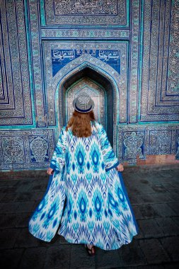Özbekistan 'ın antik Khiva kentindeki küçük kapısı ile Tash Hauli' deki mavi mozaik saray binasının iç avlusunda etnik giyinmiş kadın turist.