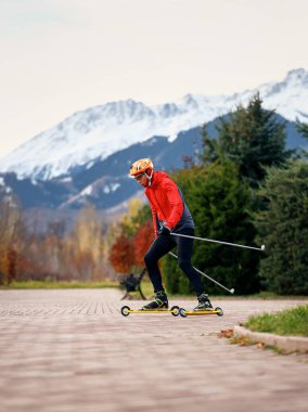 Sonbahar parkında kask ve kırmızı ceketli patenciler üzerinde antrenman yapan erkek sporcu. Kayak dağı disiplini için İskandinav kayak konsepti