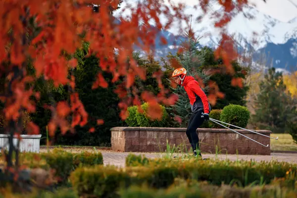 Sonbahar parkında kask ve kırmızı ceketli patenciler üzerinde antrenman yapan erkek sporcu. Kayak dağı disiplini için İskandinav kayak konsepti