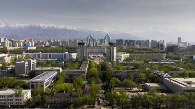İlkbaharda Kazakistan, Almaty 'de kar dağlarına karşı şehir merkezindeki Nurly Tau kompleksiyle hava aracı görüntüsü
