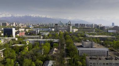 İlkbaharda Kazakistan, Almaty 'de kar dağlarına karşı şehir merkezindeki Nurly Tau kompleksiyle hava aracı görüntüsü