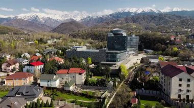 Büyük Almaty nehri ve evlerinin hava aracı manzarası, arka planda kar dağları manzaralı otel binası Kazakistan, Almaty şehrinde.