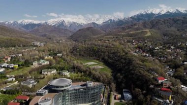 Büyük Almaty nehri ve evlerinin hava aracı manzarası, arka planda kar dağları manzaralı otel binası Kazakistan, Almaty şehrinde.