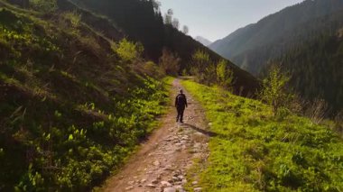 Sırt çantalı kadın yürüyüşçünün Almaty, Kazakistan 'daki yeşil orman manzarasının yakınındaki dağlarda yürüyüşünü gösteren hava görüntüsü.