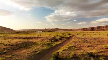 İHA, Kazakistan 'da gün batımında bulutlu gökyüzünde Ili nehri ve bahar bozkırı yakınlarında tozlu bir yol çekti.