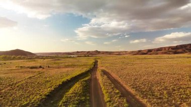 İHA, Kazakistan 'da gün batımında bulutlu gökyüzünde Ili nehri ve bahar bozkırı yakınlarında tozlu bir yol çekti.