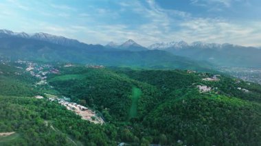 Hava aracı manzaralı evler yeşil tepe vadisi manzaralı kar dağları günbatımında gökyüzü arka planında Kazakistan, Almaty şehrinde