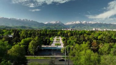 Kazakistan 'ın Almaty şehrinde mavi gökyüzü arka planında kar dağlarına karşı yeşil botanik parkı tepe manzaralı hava aracı manzarası