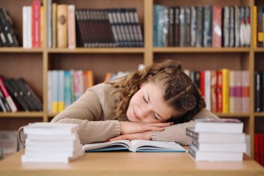 Young women got asleep on the books while studying, reading glasses on head