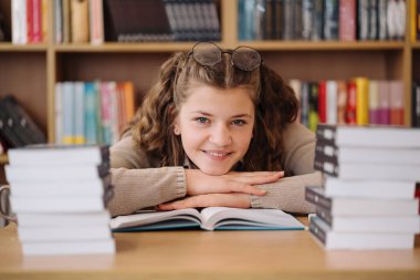 Attractive happy young girl student studying at the college library, sitting at the desk