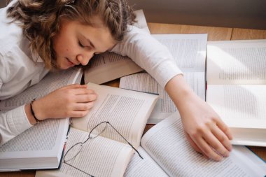 Young women got asleep on the books while studying holding reading glasses