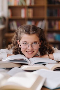 Attractive happy young girl student studying at the college library, sitting at the desk