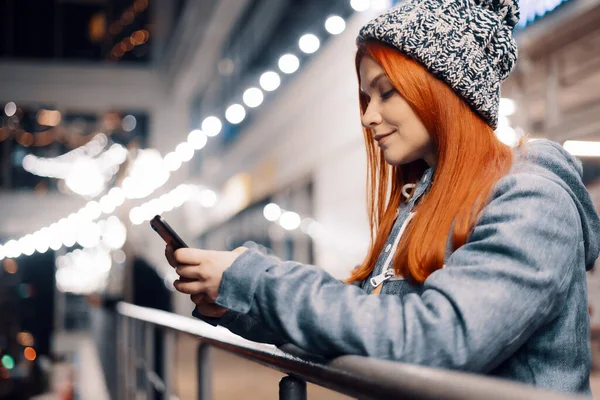美しい若い女性のスマートフォンを使用して夜の街に立って光に満ちている 携帯電話を使用した豪華な笑顔の女性の肖像 — ストック写真