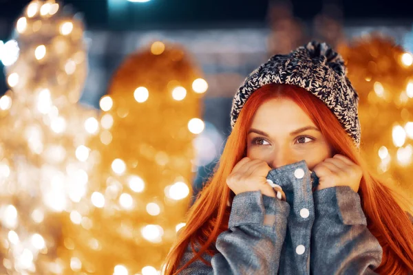 若い美しい幸せな笑顔の女の子の屋外の夜の写真お祝いの装飾を楽しんで クリスマスフェアにポーズ ヨーロッパの街の通りで ニットビーニー帽子を身に着けて — ストック写真