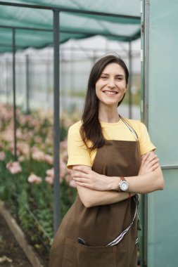 Smiling florist businesswoman portrait wearing yellow t-shirt and brown apron holding arms crossed at the green house