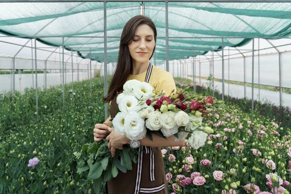 Woman florist has an order for fresh flowers. She makes a beautiful bouquet in the green house.