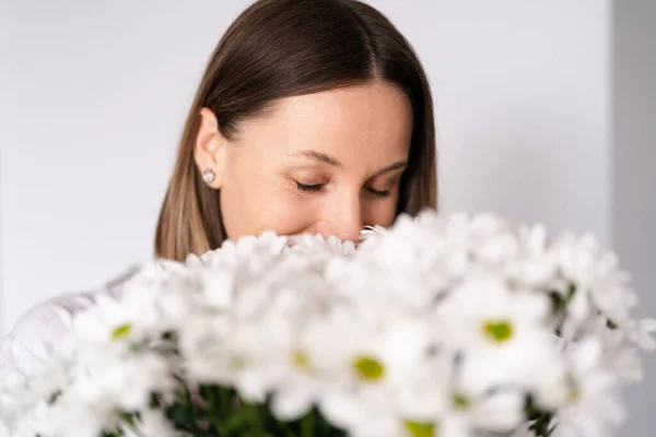Good looking Caucasian woman smells flowers, she is happy for get a fresh bouquet of white chrysanthemum