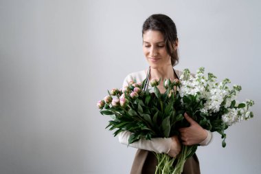 Beyaz arka planda bir demet beyaz ve pembe çiçeği kucaklayan çiçekçi kadın.