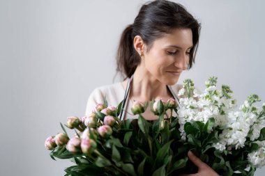 Beyaz arka planda bir demet beyaz ve pembe çiçeği kucaklayan çiçekçi kadın.