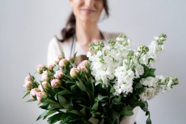 Beyaz arka planda bir demet beyaz ve pembe çiçeği kucaklayan çiçekçi kadın.