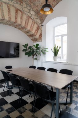 Modern bir ofis, konferans odası, içi ahşap bir masa ve pencerelerin altında duran sandalyeler. Büyük tavan ışığı.
