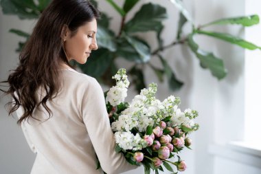 Ofisinde elinde kocaman bir buket çiçek tutan pozitif bir kadın. Doğum günü hediyesi gülümsemesi.