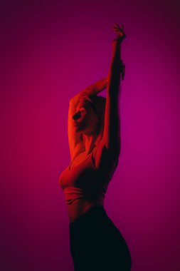 Dreamy female model closing eyes while praying for success against violet background in neon illumination