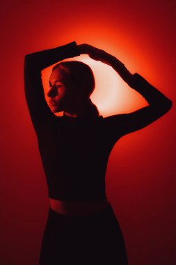 Calm female with earrings looking at camera against shiny light in dark studio with red neon illumination