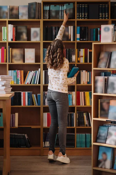 Teen girl among a pile of books. A young girl holding books with shelves in the background. She is surrounded by stacks of books. Book day.