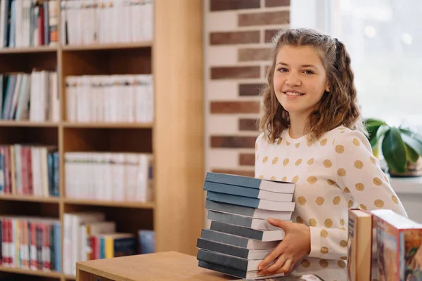 Teen girl among a pile of books. A young girl holding books with shelves in the background. She is surrounded by stacks of books. Book day.