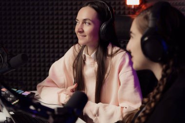 Female host and guest sitting at table with equipment while broadcasting radio program in recording studio