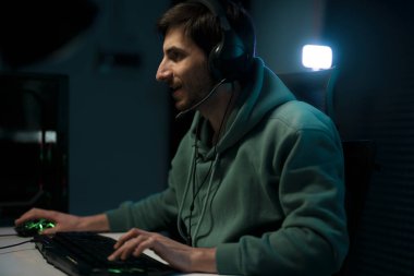 Kulaklıkla karanlık odada online video oyunu oynayan konsantre sakallı genç erkek sanal spor oyuncusunun yan görüntüsü