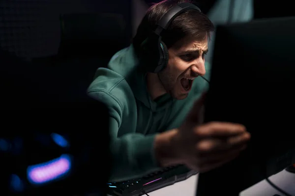 暗い部屋で成功したゲームを祝いながら ヘッドセットに触れるコンピュータモニタでのサイバースポーツゲーマー — ストック写真
