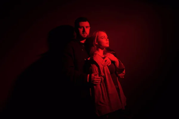 女性の後ろに立って 赤ネオンの照明で暗闇の中で優しく受け入れる若い男 — ストック写真